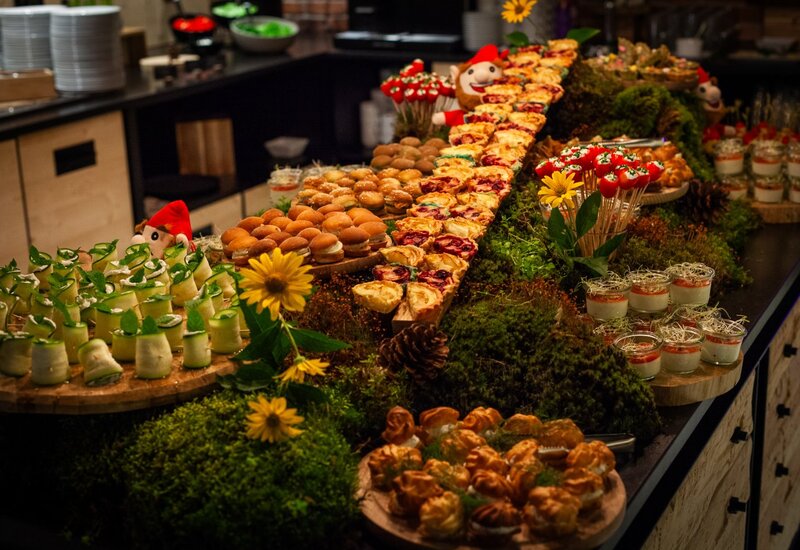 Bufet hotelowy z mini burgerami, tartami, roladkami z ogórka, deserami w słoikach i ciastkami na mchu.