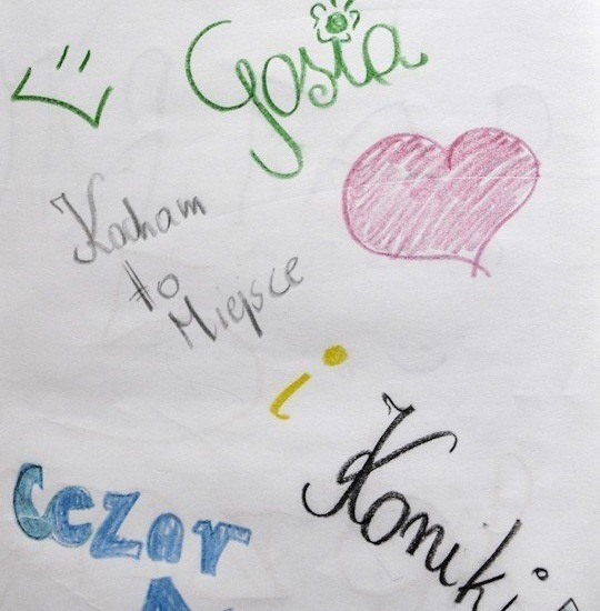 Kolorowe odręczne zapiski na kartce: 'Gosia' z kwiatkiem, różowe serce, napis 'Kocham to miejsce', niebieskie 'Cezar' i inne bazgroły.