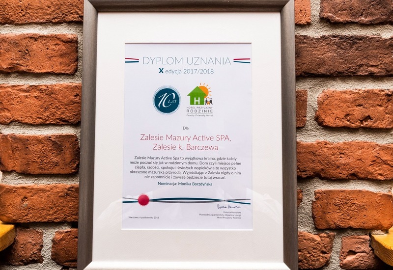 Certyfikat uznania dla Zalesie Mazury Active SPA w srebrnej ramie na ceglanej ścianie