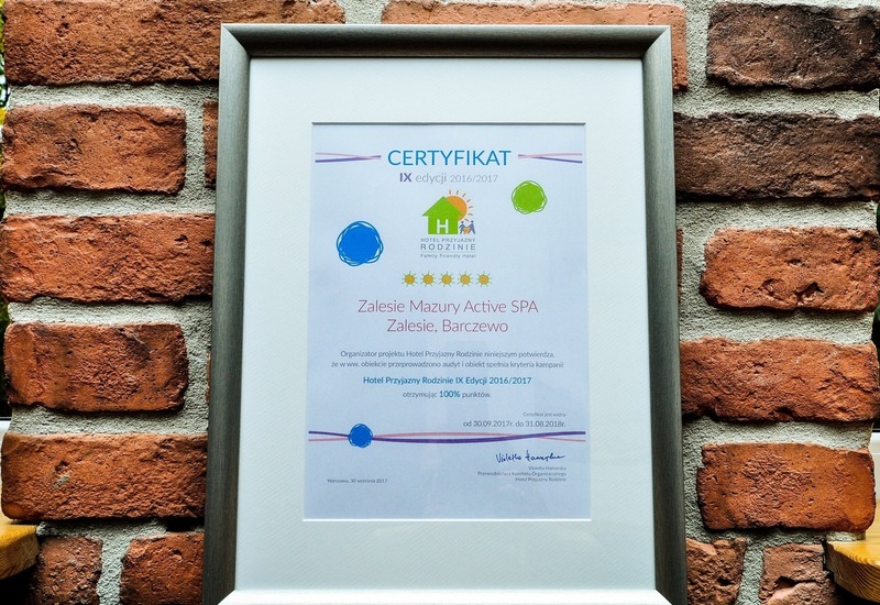 Oprawiony certyfikat Zalesie Mazury Active SPA — przyjazny rodzinom hotel i spa, srebrna ramka na ceglanej ścianie.