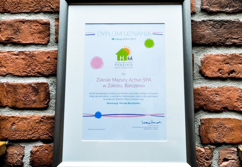 Oprawiony dyplom uznania dla Zalesie Mazury Active SPA w srebrnej ramce na ceglanym murze
