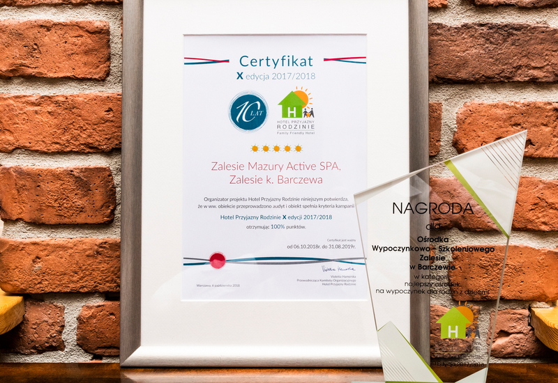 Certyfikat i szklana statuetka na blacie przy ceglanym murze, potwierdzające, że Zalesie Mazury Active SPA jest przyjazne rodzinom.