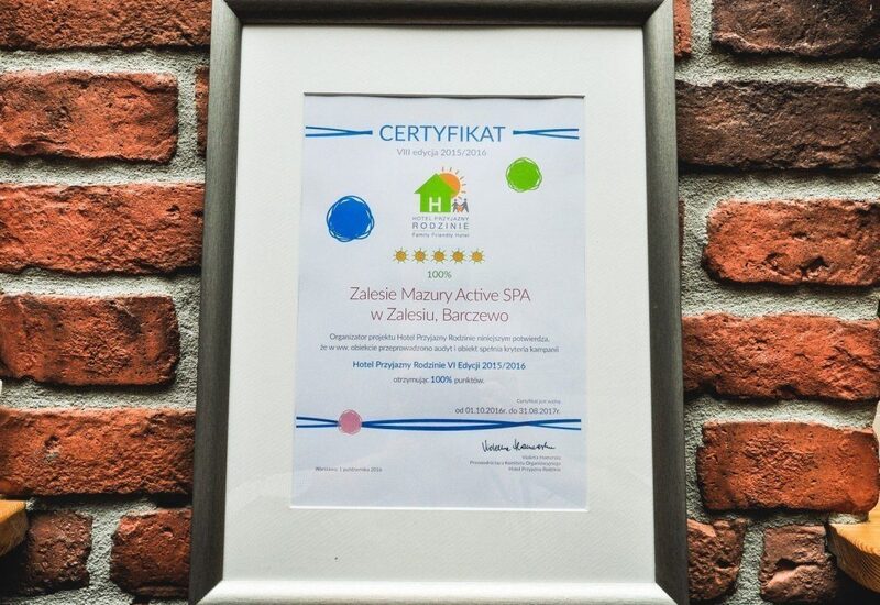 Oprawiony certyfikat przyznający Zalesie Mazury Active SPA pięć gwiazdek jako hotel przyjazny rodzinie, na rustykalnej ceglanej ścianie