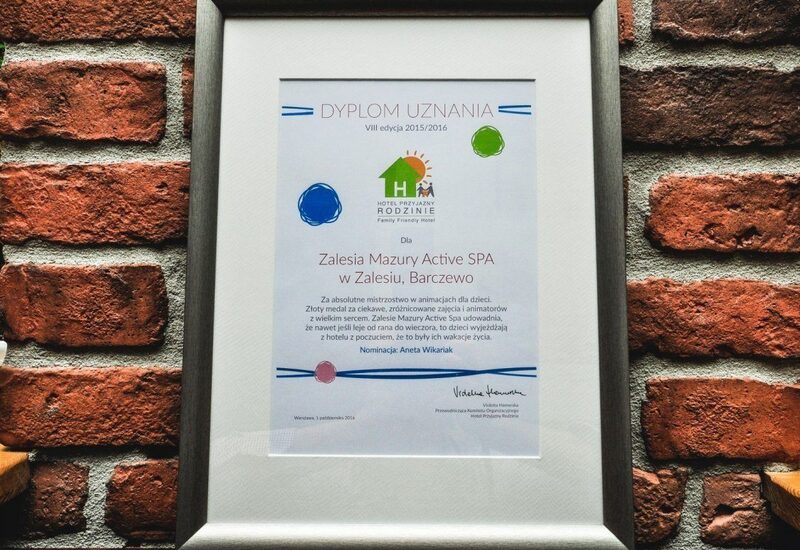 Dyplom w srebrnej ramie na ceglanej ścianie, nagroda dla Zalesia Mazury Active SPA — przyjazne rodzinom spa.