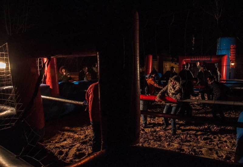 Goście grają w nadmuchiwane ludzkie piłkarzyki nocą na piaszczystej arenie, oświetlone podczas hotelowego wydarzenia.