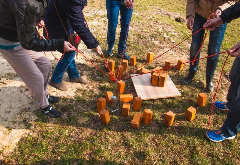Goście biorą udział w plenerowej grze integracyjnej, podnosząc i ustawiając drewniane klocki przy pomocy czerwonych lin.