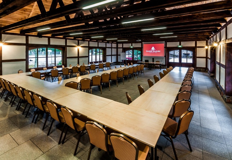 Rustykalna sala konferencyjna w Zalesie Mazury z układem stołów w U, tapicerowanymi krzesłami i odsłoniętymi belkami.