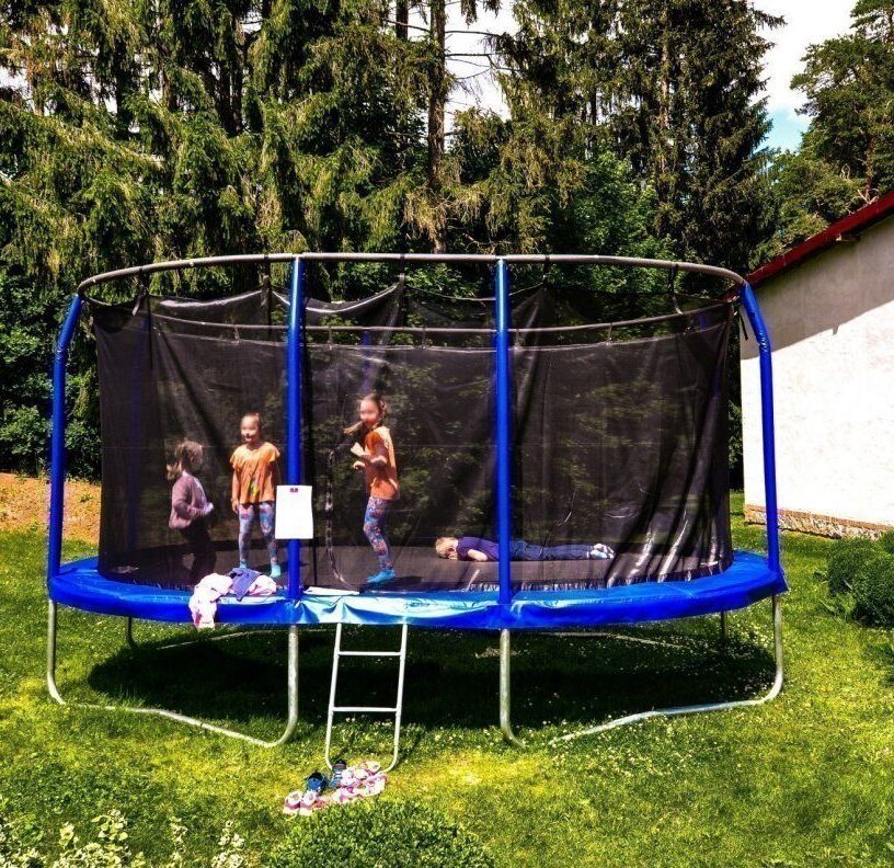 Enclosed trampoline on green lawn with children jumping and lying down; ladder and shoes at entrance