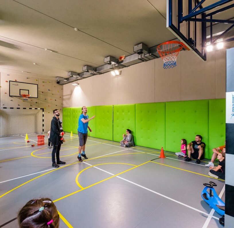 Hotel sports hall with basketball hoop, climbing wall and green padded walls; families and children playing.