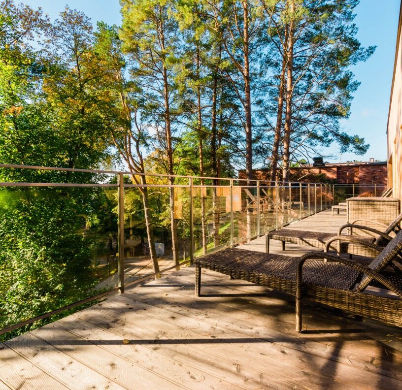 Private wooden balcony with wicker sun loungers, glass railing and treetop forest view, sunny relaxing hotel terrace.