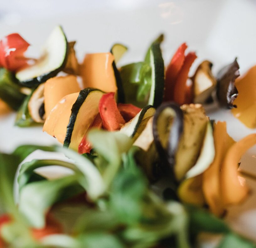 Restaurant appetizer: colorful grilled vegetable skewers with zucchini, bell peppers and mushrooms, plated with fresh greens