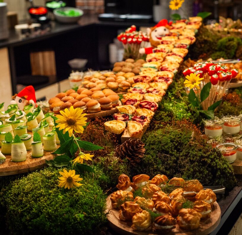 Rustic hotel buffet with assorted pastries, mini sliders, tarts and creamy desserts on moss-and-flower display.