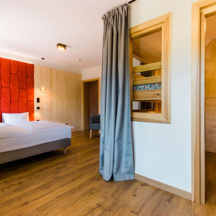 Przestronny apartament rodzinny z łóżkiem king, czerwonym tapicerowanym zagłówkiem, drewnianą podłogą i przytulną alkową dla dzieci.