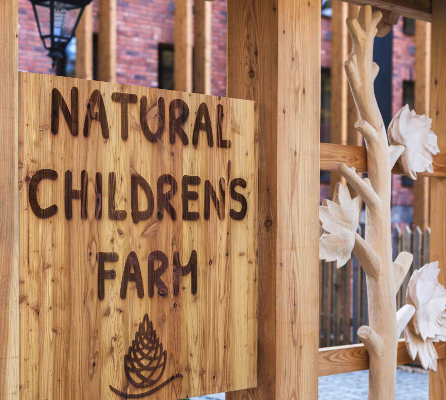 Drewniany szyld z napisem 'Natural Children's Farm' na rustykalnej ramie z rzeźbionym kwiatowym słupem
