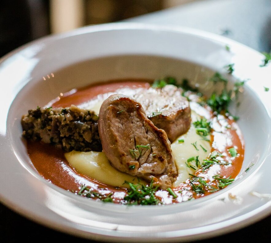 Seared pork medallions on mashed potatoes, red wine sauce, herb garnish and mushroom stuffing, plated for fine dining.