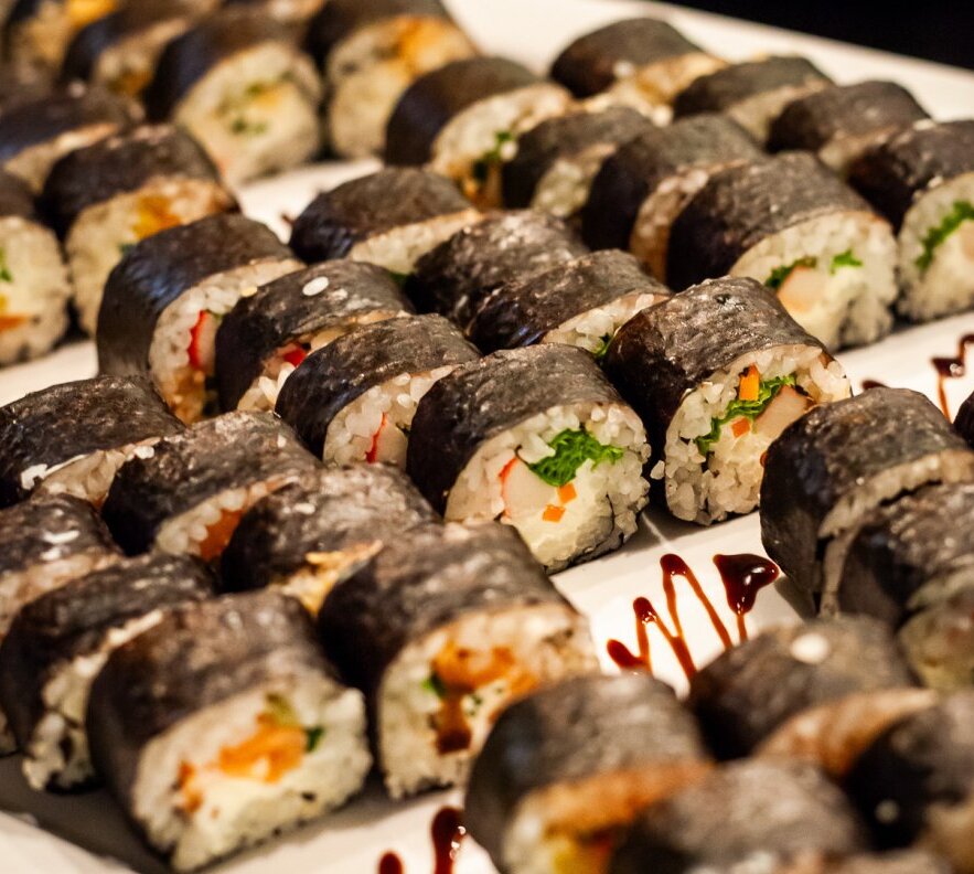 Różne rolki maki sushi owinięte nori z ryżem, warzywami i krabowym nadzieniem, estetycznie ułożone na bufetowej tacy z sosem.