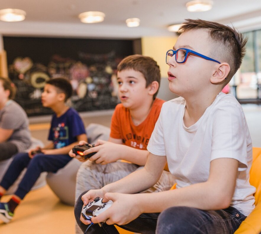Children playing video games on beanbag chairs in a family-friendly hotel game room with bright lounge and large windows