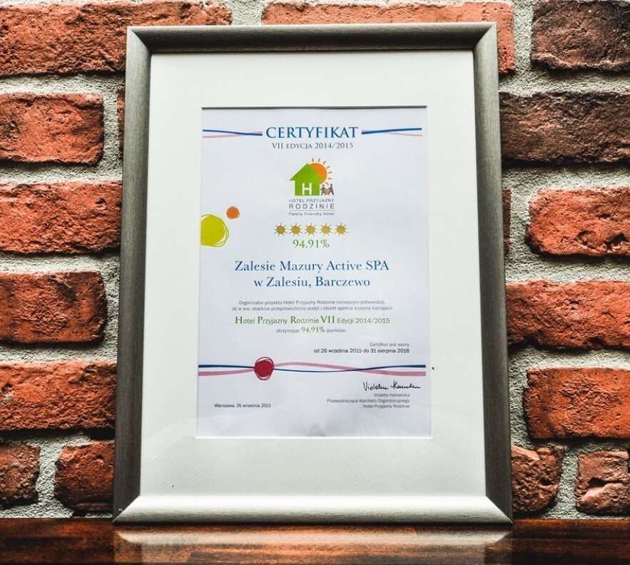 Oprawiony certyfikat hotelu Zalesie Mazury Active SPA wiszący na ceglanej ścianie nad drewnianą półką
