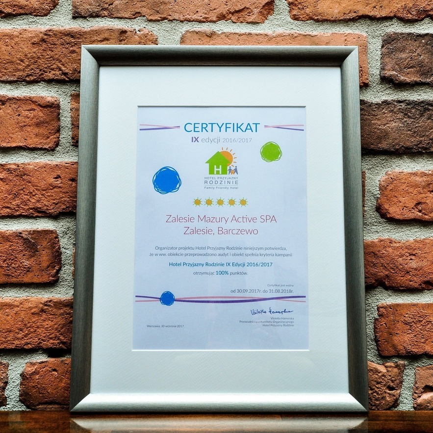 Framed accreditation for Zalesie Mazury Active SPA — five-star family-friendly hotel and spa, silver frame on exposed brick.