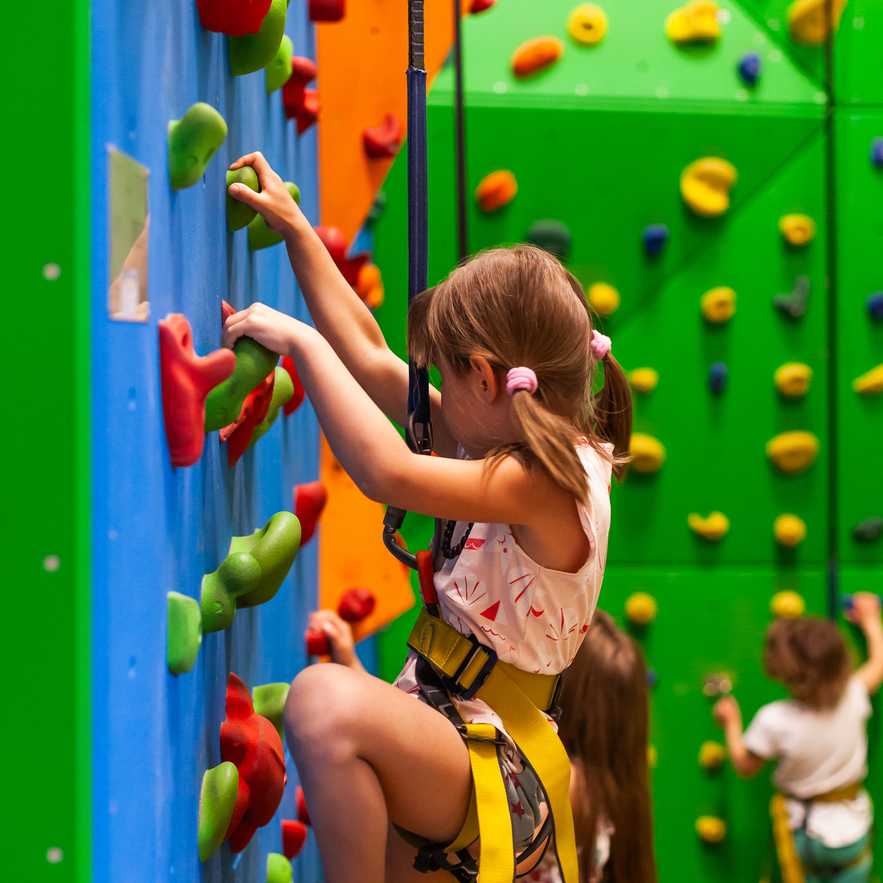 Colorful indoor climbing wall with children in safety harnesses enjoying a supervised kids' activity area