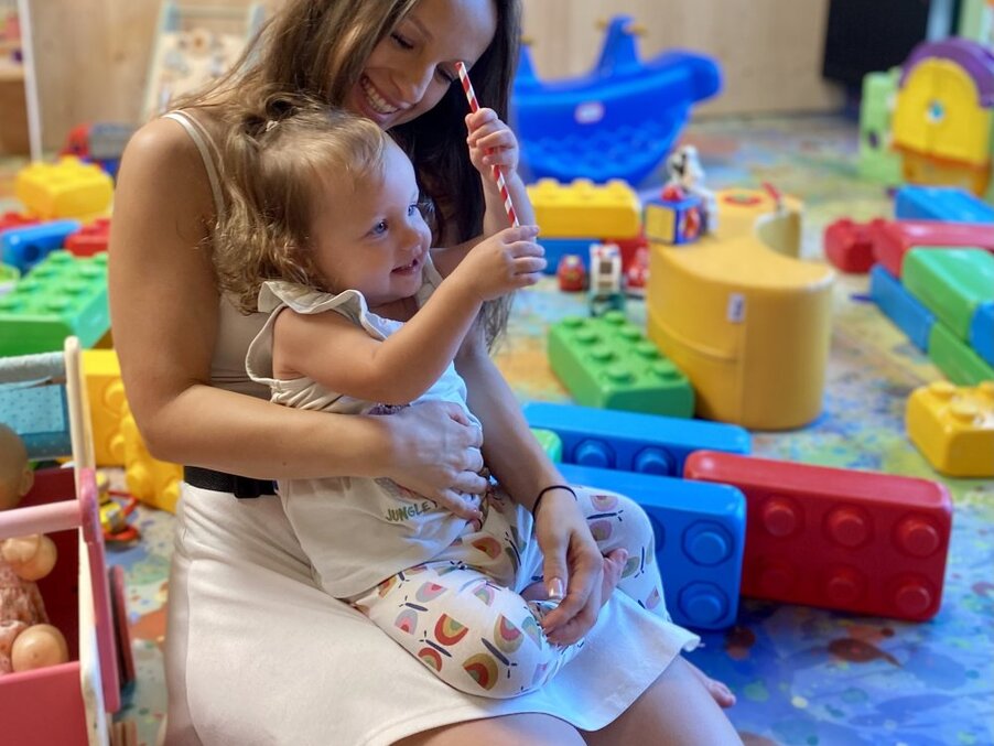 Smiling mother holding toddler in a bright family playroom with colorful foam building blocks and toys — hotel kids' club area.