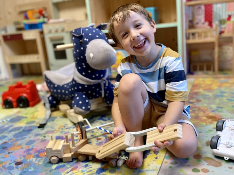 Smiling child playing with a wooden toy truck in a colorful hotel kids' playroom with a polka-dot rocking horse