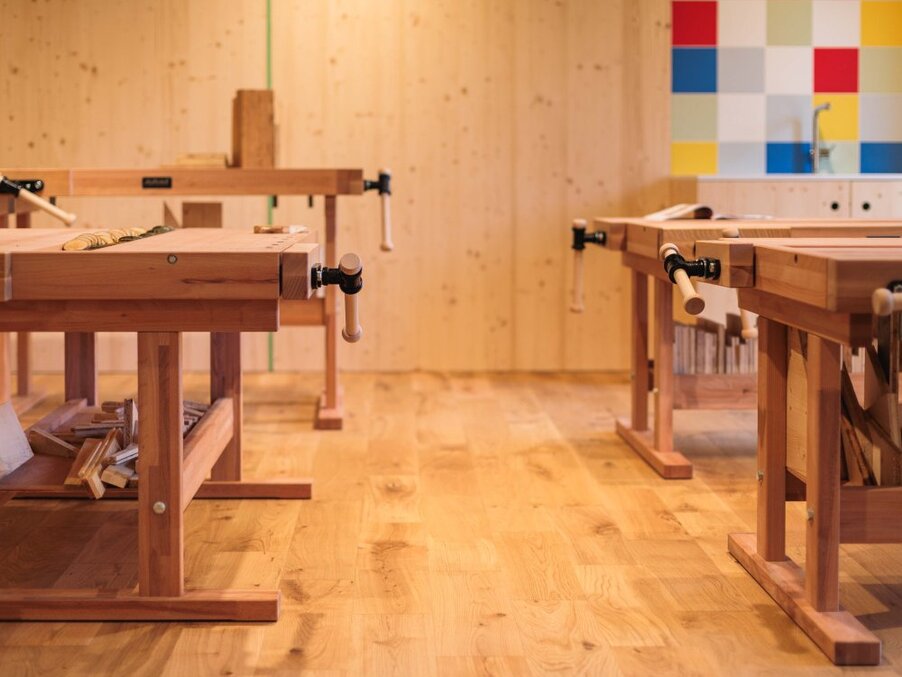 Wood-panel craft room with solid wooden workbenches, hand vises and tools, warm lighting and colorful tiled sink area