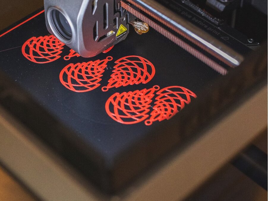 Dysza drukarki 3D nakłada czerwone, ażurowe wzory kolczyków na podgrzewaną czarną platformę roboczą