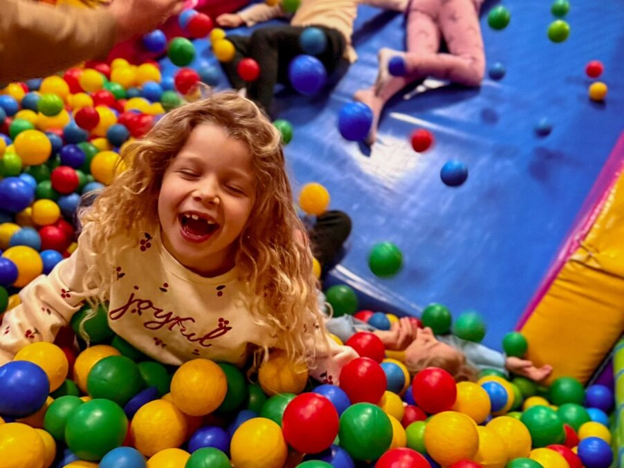Laughing child playing in colorful indoor ball pit at hotel's kids' club, vibrant and safe family-friendly play area.
