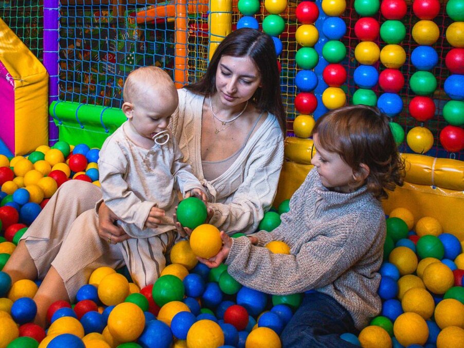 Mother with toddler and young child playing in a colorful indoor ball pit at the hotel's family play area.