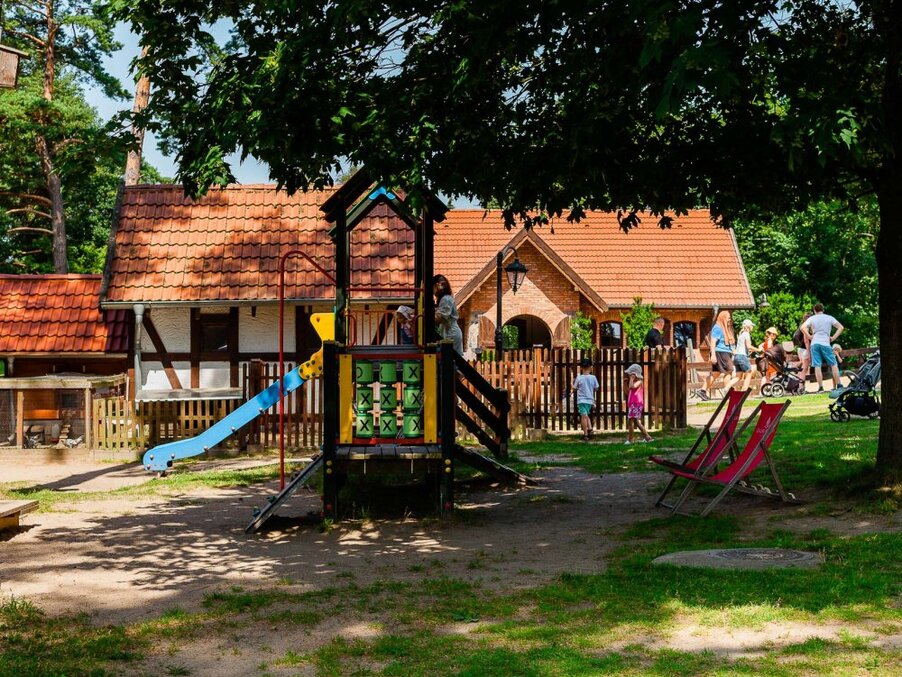 Playground with slide and tic-tac-toe panel, shaded lawn with deck chairs and rustic red-tiled guest cottages nearby