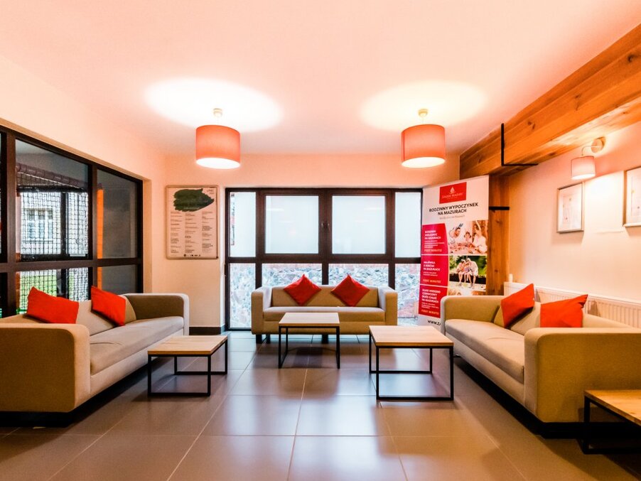 Contemporary hotel lounge with three sofas, red accent cushions, coffee tables, warm pendant lights and large windows