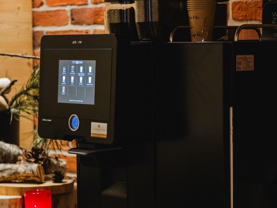 Self-service coffee machine with touchscreen and paper cups in cozy brick-walled hotel breakfast area