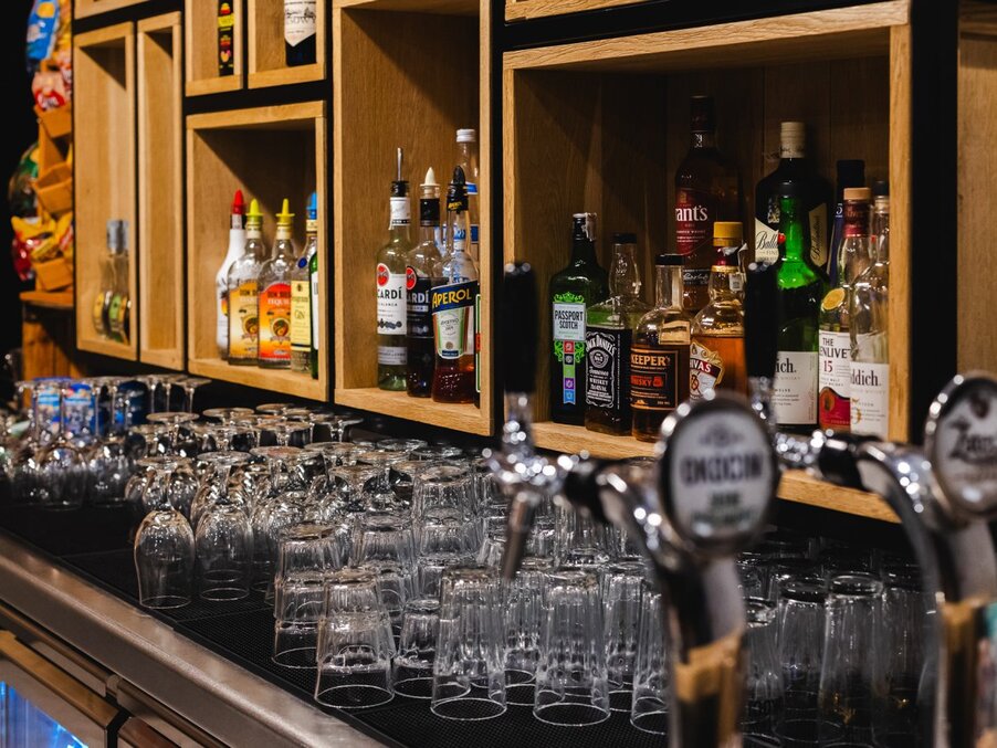 Hotel bar counter with rows of inverted glassware, warm wooden shelving of spirits and beer taps ready for service