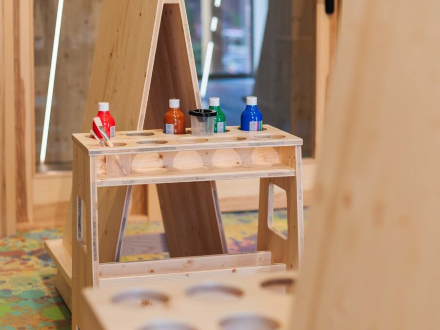 Children's wooden craft station with A-frame easel, jars of colorful paint and brushes in a family-friendly hotel play area.
