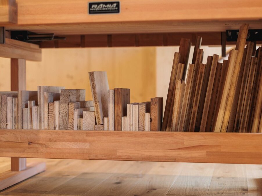 Neatly arranged wooden flooring and trim samples under a workbench, assorted plank sizes and natural wood grains