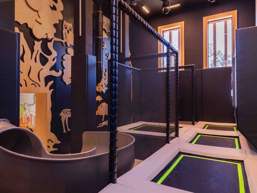 Hotel kids' playroom with multiple recessed trampolines, curved slide, safety netting, padded walls and wood-framed windows