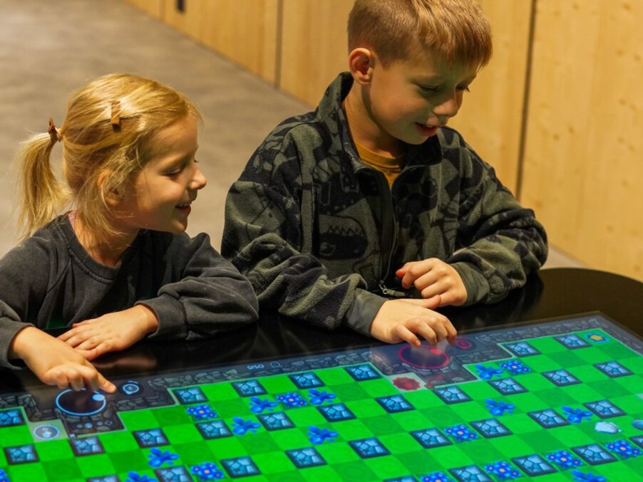 Two children playing an interactive touchscreen game on a brightly colored table in a family-friendly hotel play area.