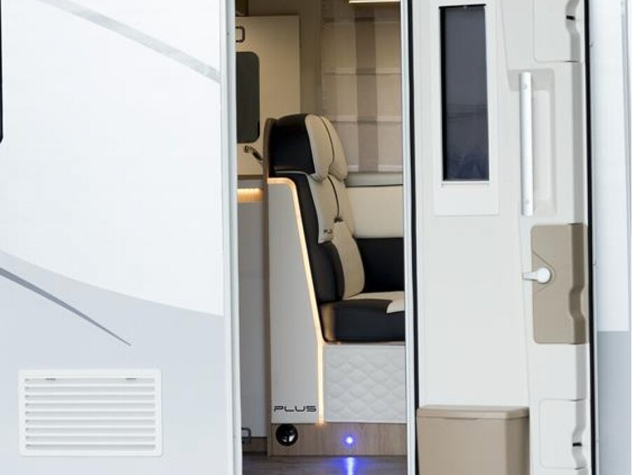 Motorhome entrance with luxury leather captain seat, quilted storage base, warm LED lighting and a view of the compact kitchenette.