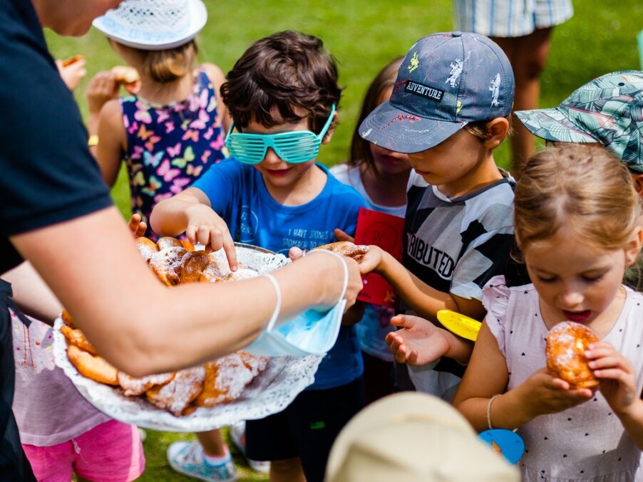 Children at a hotel garden party reaching for powdered pastries on a platter during a family-friendly outdoor activity.