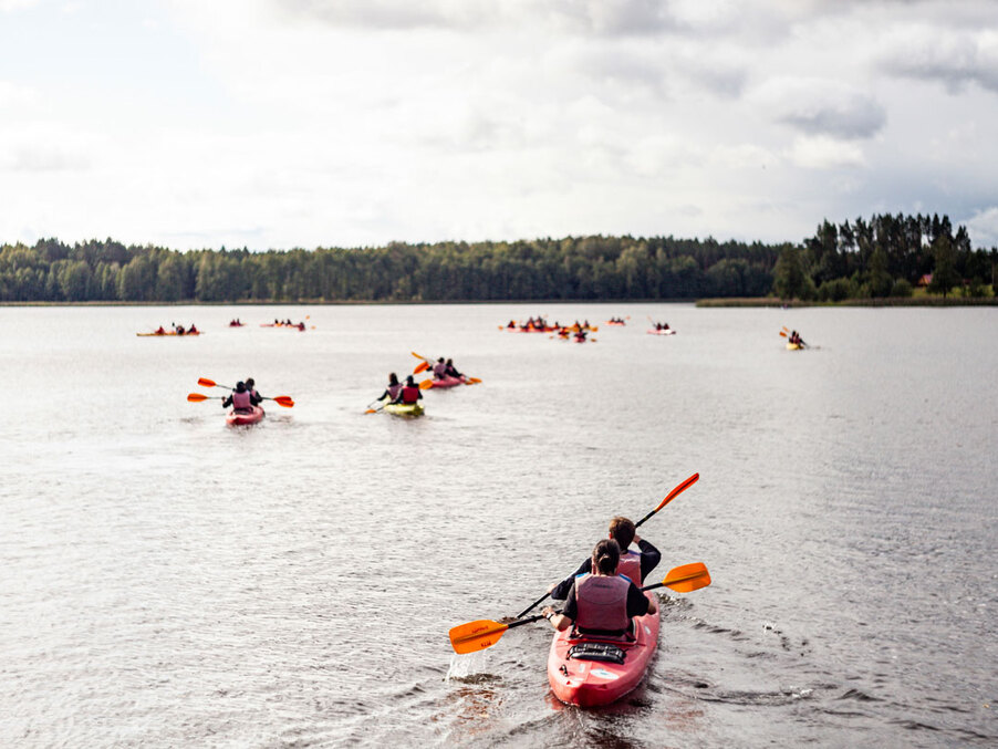 Guests kayaking in tandem on a calm lake during a guided group tour, orange paddles and forested shoreline in the distance