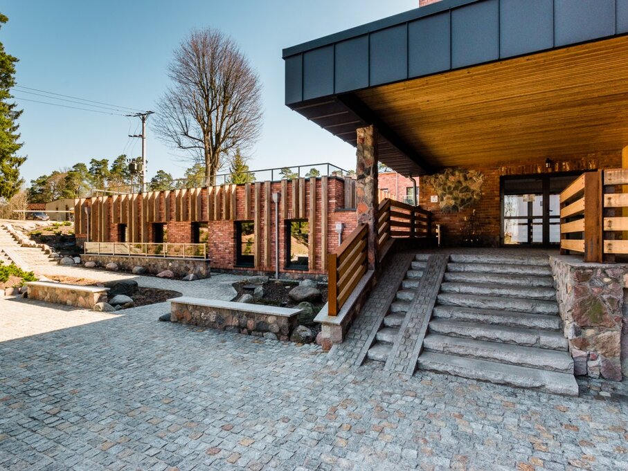 Covered hotel entrance with wooden ceiling, stone steps and ramp, brick façade, paved courtyard and landscaped rock beds.