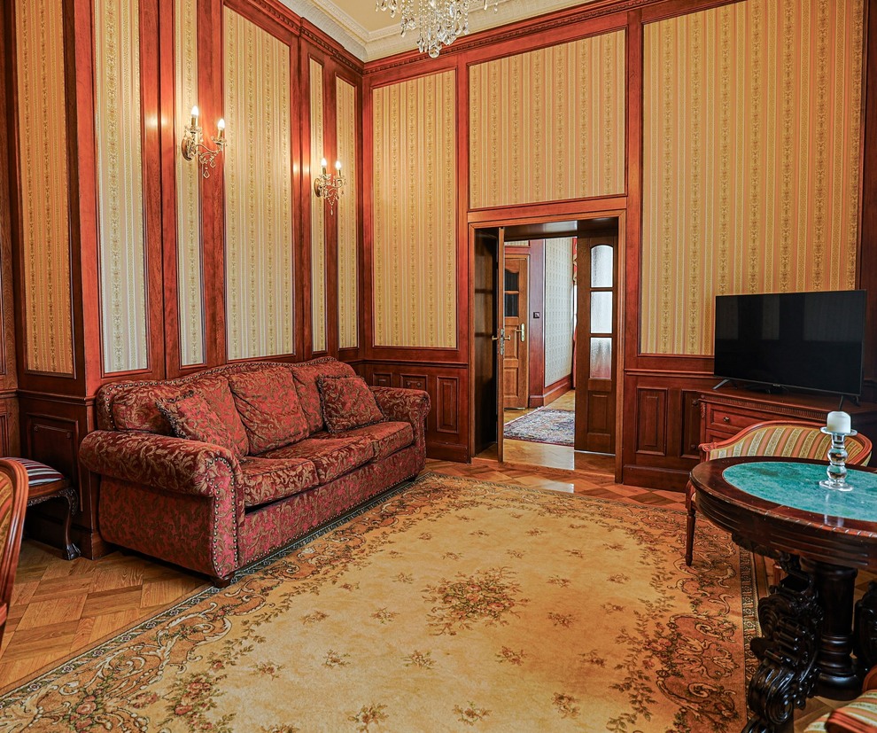 Elegancki klasyczny salon hotelowy z boazerią, wzorzystą tapetą, kryształowym żyrandolem, bordową sofą, okrągłym stolikiem i telewizorem
