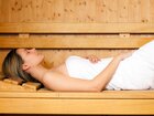 Gość wypoczywa na drewnianej ławce sauny, owinięty białym ręcznikiem, z zamkniętymi oczami na podgłówku w strefie spa