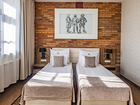 Jasny pokój hotelowy z dwoma pojedynczymi łóżkami, ceglanym akcentem, tapicerowanymi zagłówkami, lampkami nocnymi i dużym oknem.