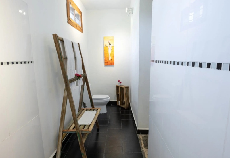 Minimalist bathroom with black tile floor, white walls, small window, towel rack with white towels, and decorative wall art