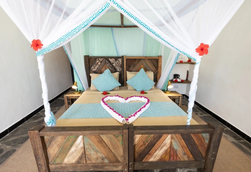 Cozy rustic wooden bed with light blue patterned pillows and canopy draped with white fabric, decorated with rose petals in heart shape