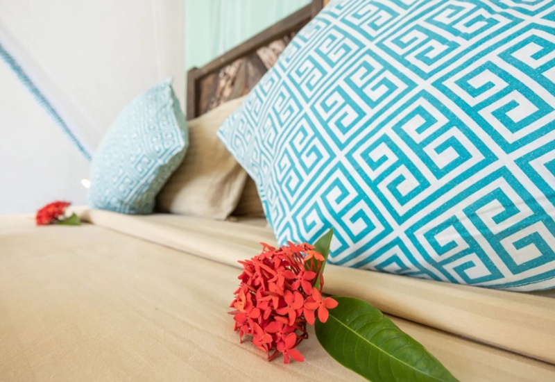 Beige bed with decorative blue geometric pillows and red flower on soft beige sheets in a relaxing hotel room