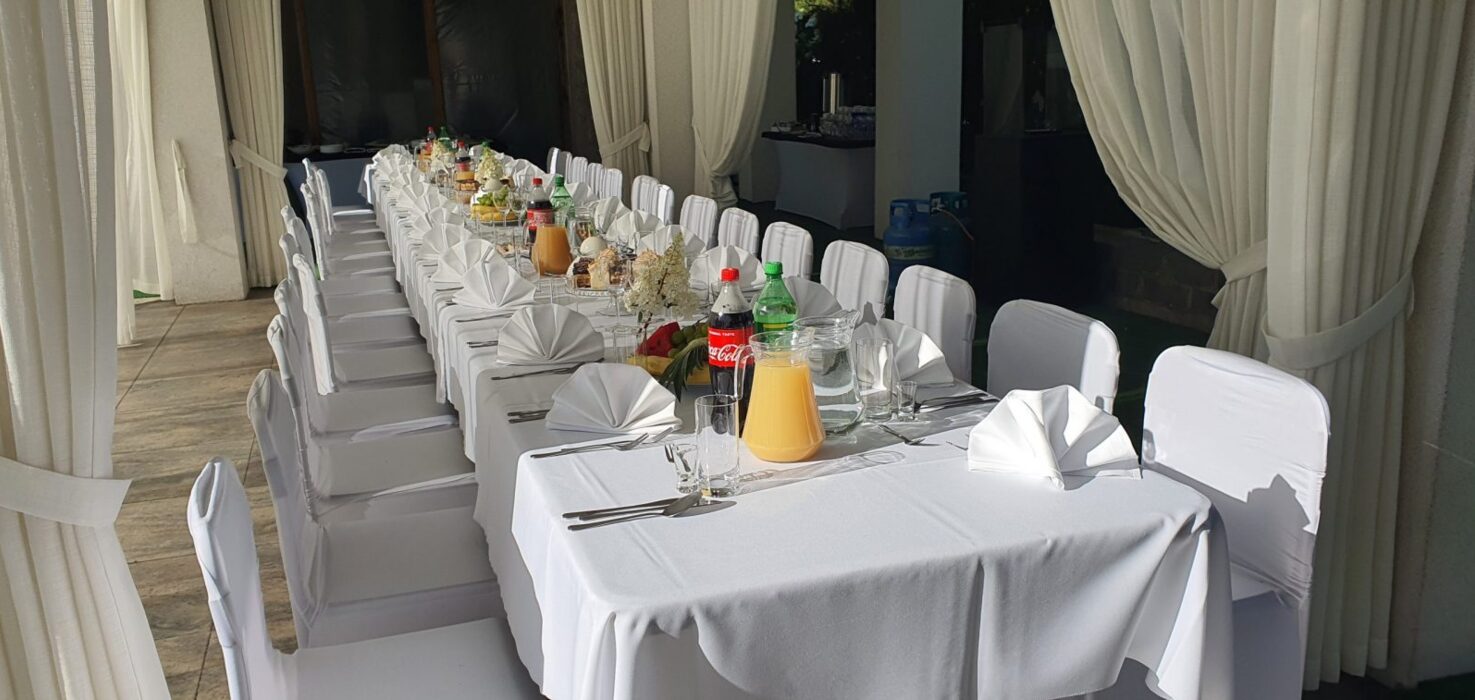 Długi stół bankietowy przyjęty na zewnątrz z białymi pokrowcami na krzesłach, serwetkami, napojami i przekąskami