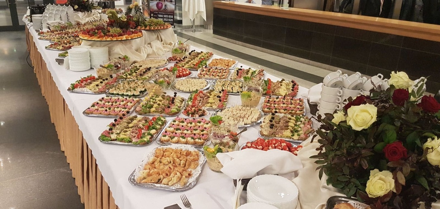 Bogato zastawiony bufet z różnorodnymi przekąskami, sałatkami i owocami, udekorowany kwiatami, gotowy na przyjęcie gości w hotelu.